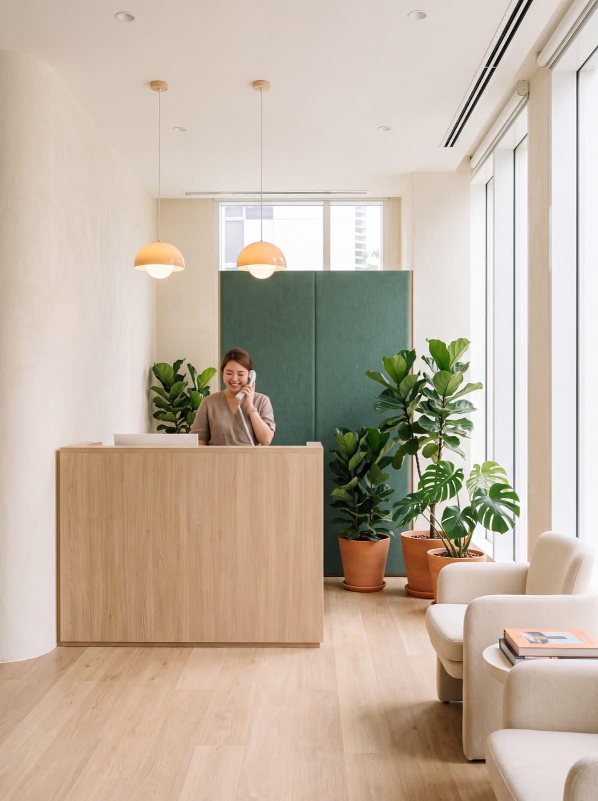 A clinic receptionist answering the phone at a pale oak reception desk.