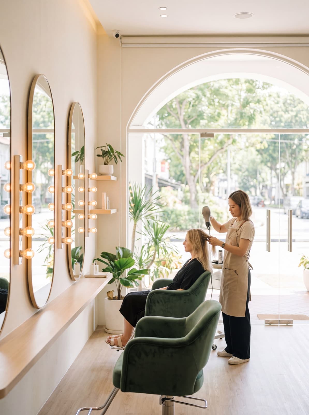 A stylist finishing a blow-dry in a bright salon with jade chairs.